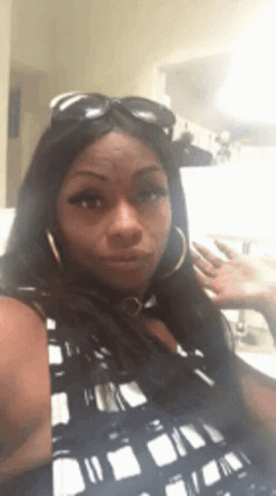 A Woman Wearing Sunglasses And Hoop Earrings Is Making A Funny Face GIF