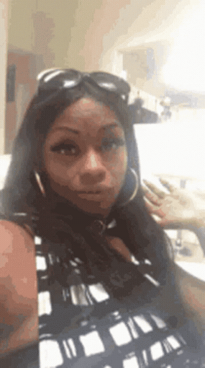 A Woman Wearing Sunglasses And Hoop Earrings Is Taking A Selfie GIF