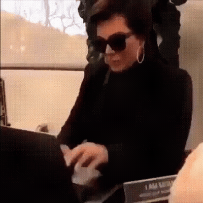 A Woman Wearing Sunglasses And Hoop Earrings Is Typing On A Laptop Computer . GIF