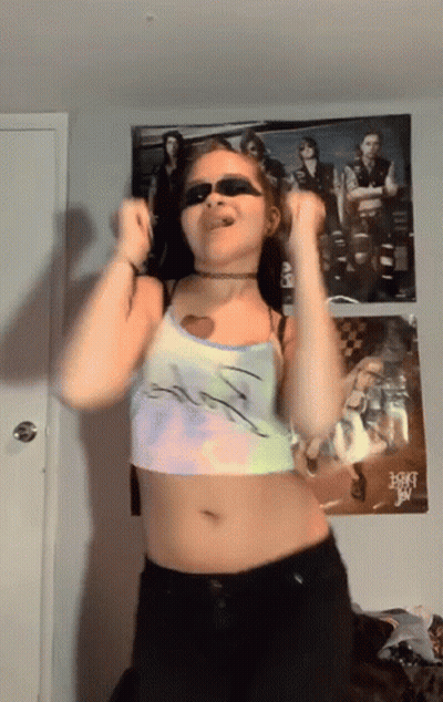 A Woman Wearing Sunglasses Is Dancing In Front Of A Poster Of A Band Called A-Ha GIF