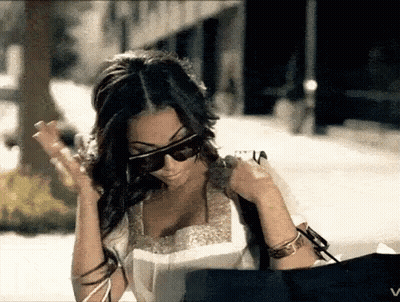 A Woman Wearing Sunglasses Is Holding A Bag And Looking At Something GIF