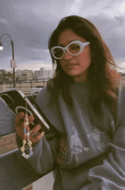 A Woman Wearing Sunglasses Is Holding A Cell Phone In Her Hand GIF