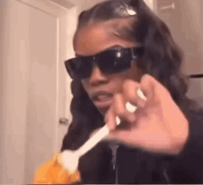 A Woman Wearing Sunglasses Is Holding A Spoon In Her Hand And Making A Funny Face . GIF