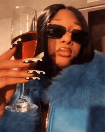 A Woman Wearing Sunglasses Is Holding A Wine Glass GIF