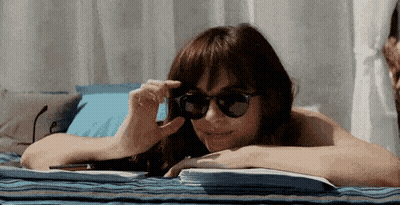 A Woman Wearing Sunglasses Is Laying On A Towel On A Beach . GIF