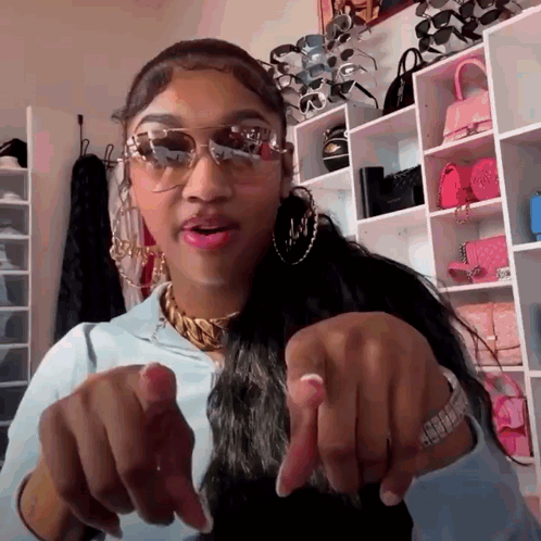 A Woman Wearing Sunglasses Is Pointing At The Camera With Her Fingers GIF