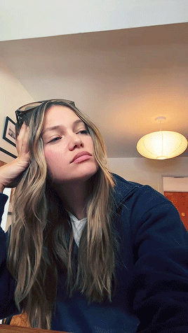 A Woman Wearing Sunglasses Is Sitting At A Table With Her Hand On Her Face GIF