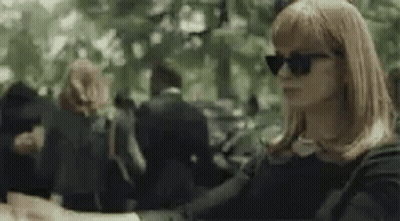 A Woman Wearing Sunglasses Is Sitting In A Park . GIF