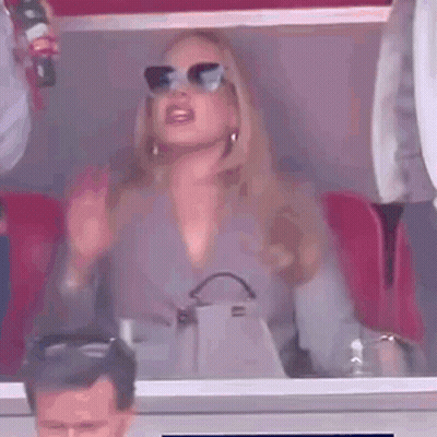 A Woman Wearing Sunglasses Is Sitting In A Stadium Holding A Bottle Of Coca Cola . GIF