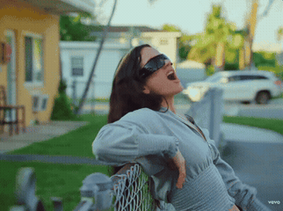 A Woman Wearing Sunglasses Is Sitting On A Chain Link Fence With Her Mouth Open GIF