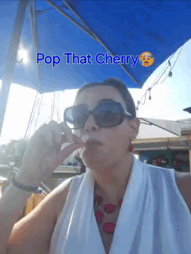 A Woman Wearing Sunglasses Is Sitting Under An Umbrella With The Words Pop That Cherry Written Above Her GIF