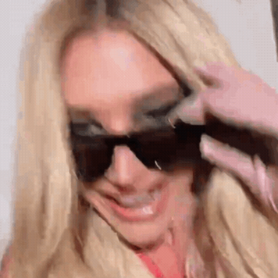 A Woman Wearing Sunglasses Is Smiling And Making A Funny Face . GIF