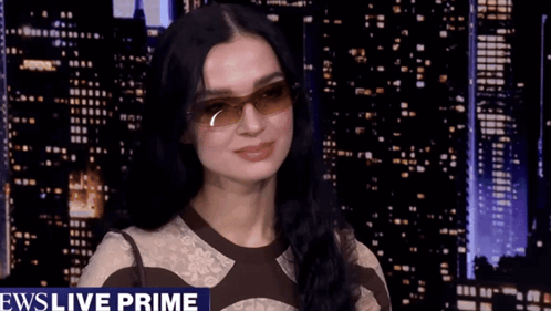 A Woman Wearing Sunglasses Is Smiling In Front Of A News Live Prime Banner GIF