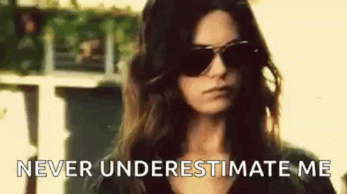 A Woman Wearing Sunglasses Is Standing In Front Of A Building And Saying `` Never Underestimate Me '' . GIF