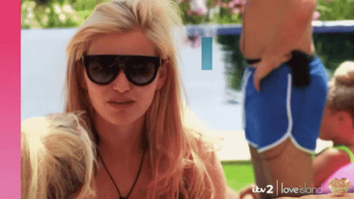 A Woman Wearing Sunglasses Is Standing In Front Of A Man In Blue Shorts GIF