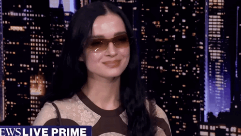 A Woman Wearing Sunglasses Is Standing In Front Of A News Live Prime Banner GIF