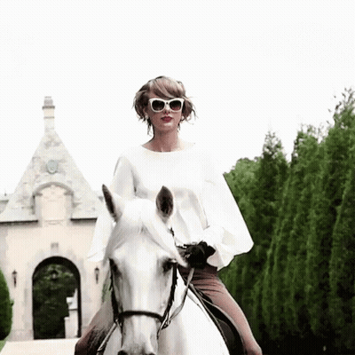 A Woman Wearing Sunglasses Rides A White Horse In Front Of A Building GIF