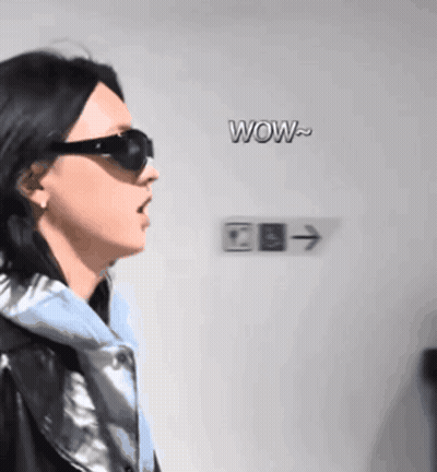 A Woman Wearing Sunglasses Stands In Front Of A Sign That Says Wow On It GIF