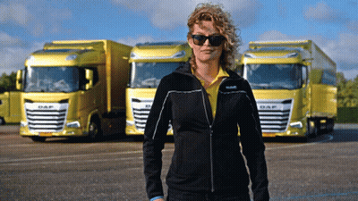 A Woman Wearing Sunglasses Stands In Front Of Yellow Daf Trucks GIF