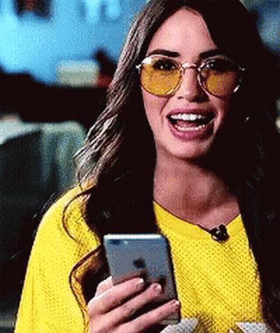 A Woman Wearing Yellow Sunglasses And A Yellow Shirt Is Holding A Cell Phone . GIF