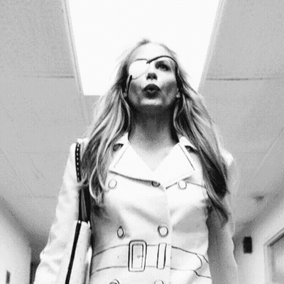 A Woman With A Bandage On Her Eye Is Walking Down A Hallway With A Purse . GIF