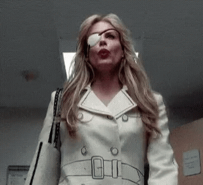 A Woman With A Bandage On Her Eye Is Wearing A White Trench Coat And Sunglasses . GIF