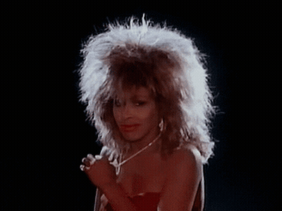 A Woman With A Big Afro Is Singing Into A Microphone While Wearing A Red Dress And A Necklace . GIF
