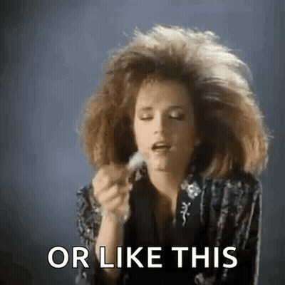 A Woman With A Big Hairdo Is Holding A Feather In Her Hand And Saying Or Like This . GIF