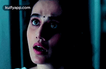 A Woman With A Bindi On Her Forehead Is Looking At The Camera In The Dark . GIF