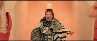 A Woman With A Box On Her Head Is Wearing A Striped Outfit GIF