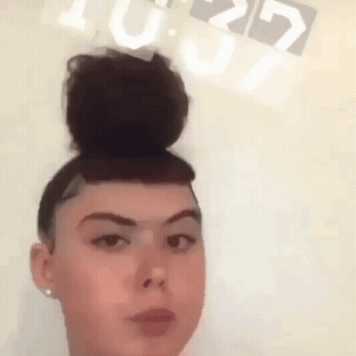 A Woman With A Bun On Her Head Is Standing In Front Of A Clock That Reads 10:29 GIF