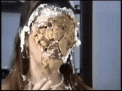 A Woman With A Cake On Her Face Is Sitting In Front Of A Window . GIF