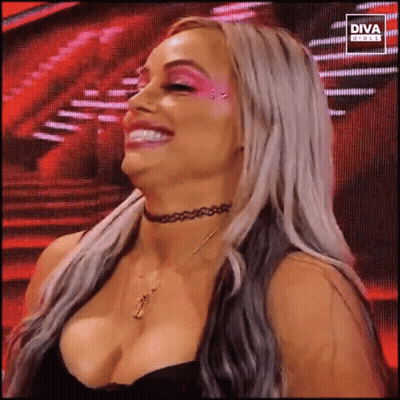 A Woman With A Choker Around Her Neck Is Smiling While Standing In Front Of A Large Screen . GIF