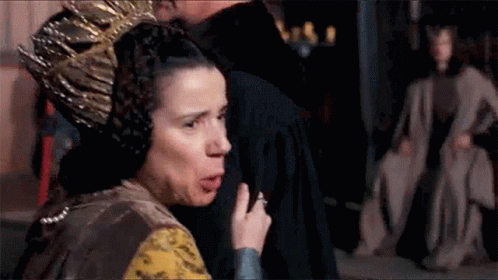 A Woman With A Crown On Her Head Is Standing Next To A Man In A Room . GIF