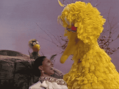 A Woman With A Crown On Her Head Stands Next To A Big Bird GIF