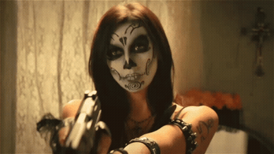A Woman With A Day Of The Dead Makeup On Her Face Holds A Gun GIF