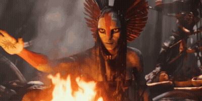 A Woman With A Feathered Headdress Is Standing In Front Of A Fire GIF