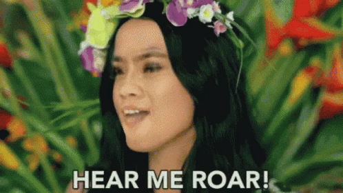 A Woman With A Flower Crown On Her Head Is Standing In Front Of A Flower Garden . GIF