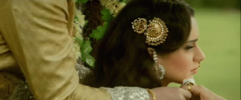 A Woman With A Flower In Her Hair Is Being Held By A Man In A Gold Suit GIF