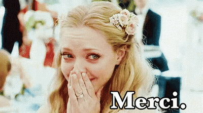 A Woman With A Flower In Her Hair Is Covering Her Face With Her Hands And The Word Merci Is On The Bottom GIF
