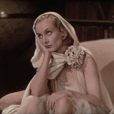 A Woman With A Flower In Her Hair Is Sitting In A Chair With Her Hand On Her Face GIF