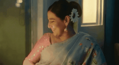 A Woman With A Flower In Her Hair Is Smiling While Holding A Baby . GIF