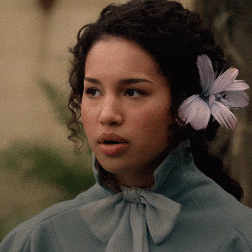 A Woman With A Flower In Her Hair Is Wearing A Blue Shirt GIF