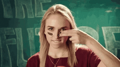 A Woman With A Football On Her Face Is Smiling And Covering Her Nose With Her Hand . GIF