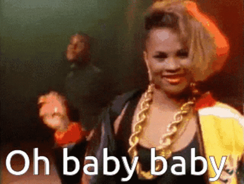 A Woman With A Gold Chain Around Her Neck Is Smiling With The Words Oh Baby Baby Below Her GIF
