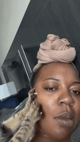 A Woman With A Head Scarf On Her Head Is Being Petted By A Cat GIF