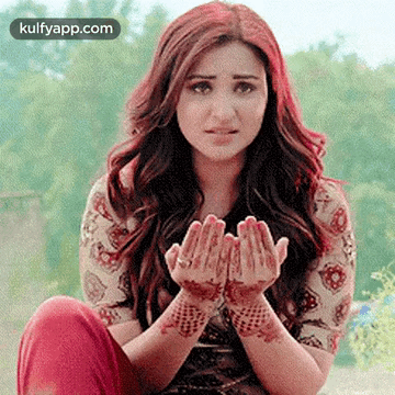 A Woman With A Henna Tattoo On Her Hands Is Sitting On The Ground With Her Hands Folded In Prayer . GIF