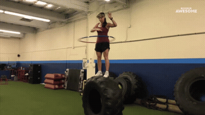 A Woman With A Hula Hoop On Top Of A Tire In A Gym With The Words Awesome Behind Her GIF