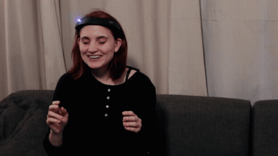 A Woman With A Light On Her Head Is Smiling GIF
