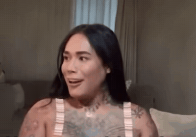 A Woman With A Lot Of Tattoos Is Sitting On A Couch And Smiling . GIF
